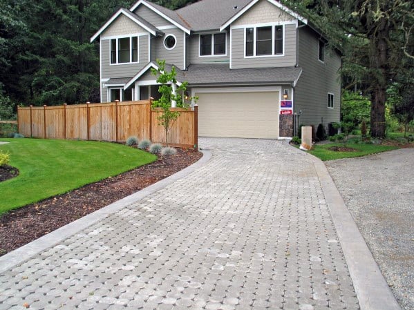 Permeable paver driveway with concrete edging leading to a gray two-story house and fenced yard.