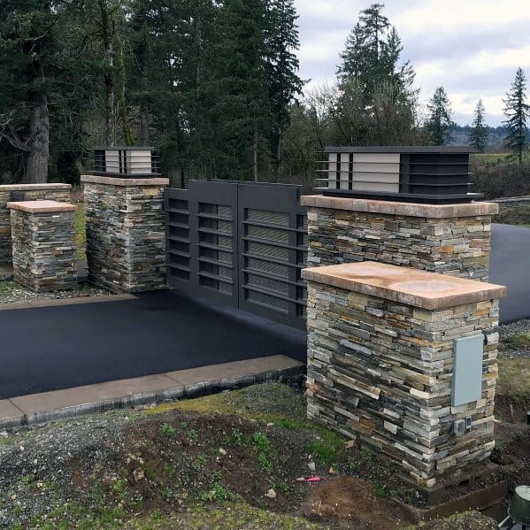 Modern driveway gate with horizontal metal slats and stacked stone pillars with caps.