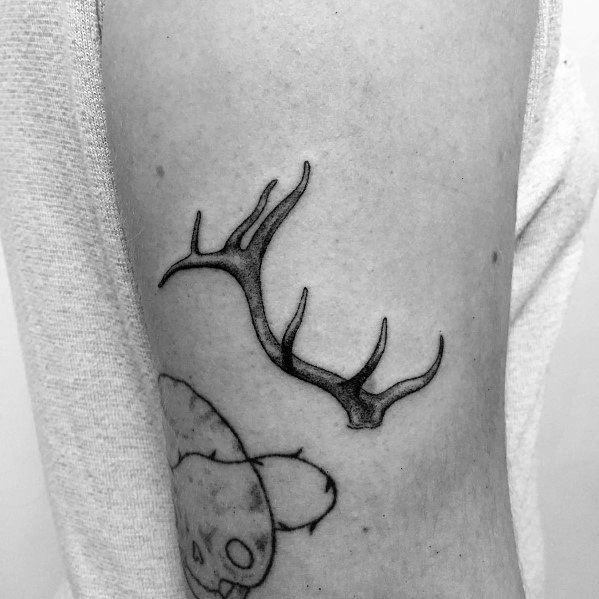 Small black and grey elk antler tattoo on the upper arm, featuring fine lines and subtle shading for a minimalist and natural look.