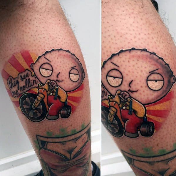 Tattoo of Stewie Griffin from Family Guy riding a tricycle with a mischievous grin, set against a sunburst background with "they see me rollin" text.