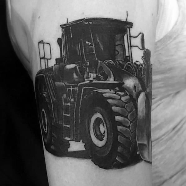 Hyper-realistic black and gray tattoo of a large tractor with detailed tire treads and shading on the upper arm.