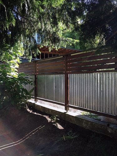 Corrugated metal fence with wooden slats on top, providing backyard privacy in a shaded area.