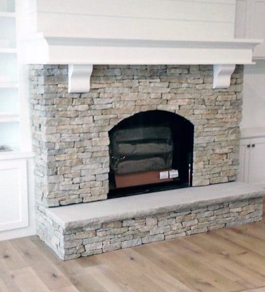 Stone fireplace with an arched opening, white wood mantel, and decorative corbels.