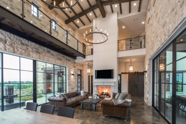 Spacious living room with high ceiling, stone walls, leather sofas, concrete floor, fireplace, and large windows