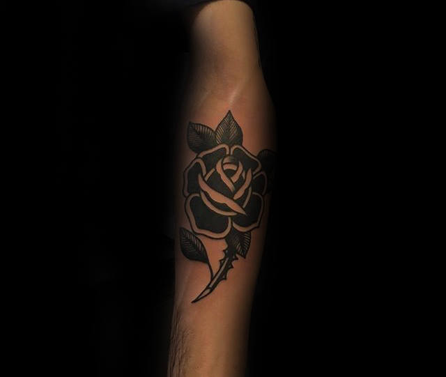 Black rose tattoo with leaves on a forearm