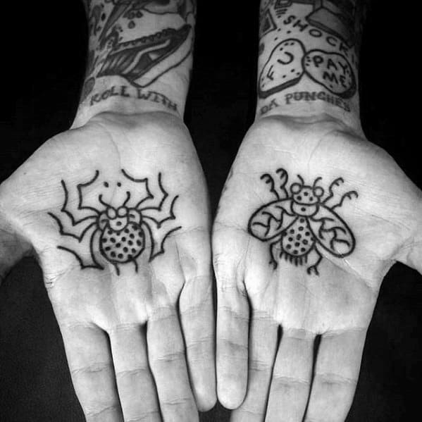 Minimalist spider and fly tattoos on each palm, drawn in a bold, cartoon-like style with dot and line detailing.