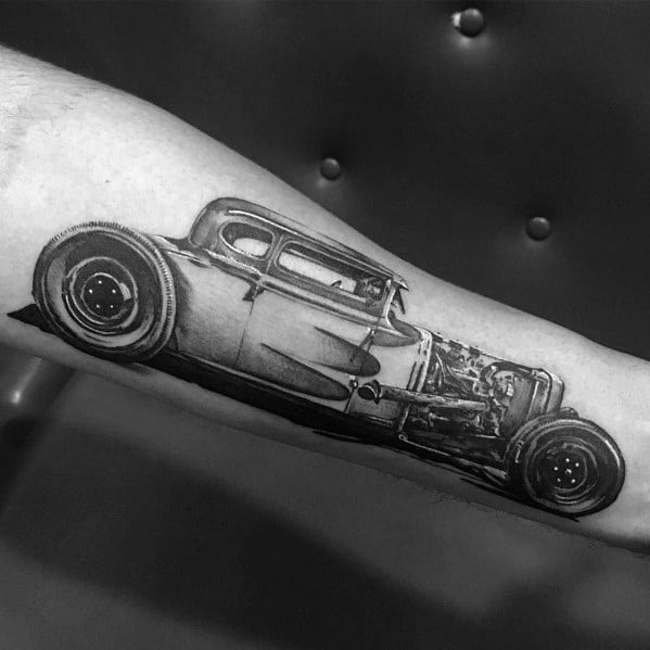 Realistic black and grey Ford hot rod tattoo on forearm, featuring detailed shading, exposed engine, and a vintage classic car design.