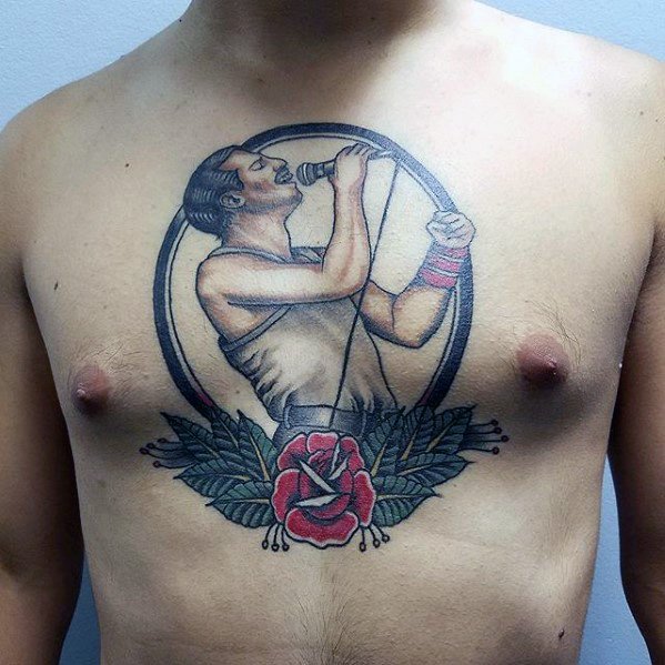 Chest tattoo of Freddie Mercury singing into a mic, framed in a circle with bold outlines and a red rose with leaves below.