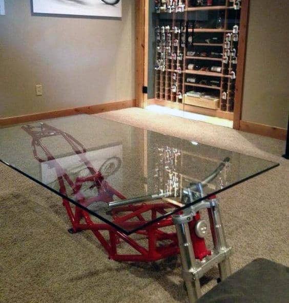 Glass coffee table with a red motorcycle frame base in a room with a wine rack