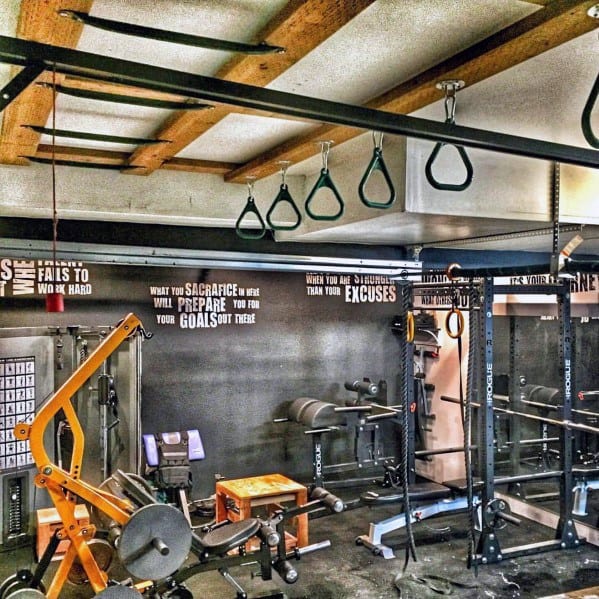 Industrial-style garage gym with pull-up bars, fitness equipment, and motivational wall quotes.