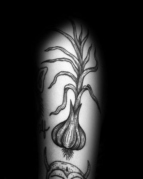 Black and grey garlic tattoo with long stems and roots, featuring fine linework and shading for a botanical-inspired design.