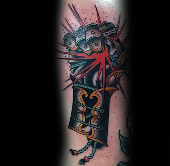 Bold tattoo of a clenched armored gauntlet with red burst lines, detailed with gold accents and a rope-tied cuff.