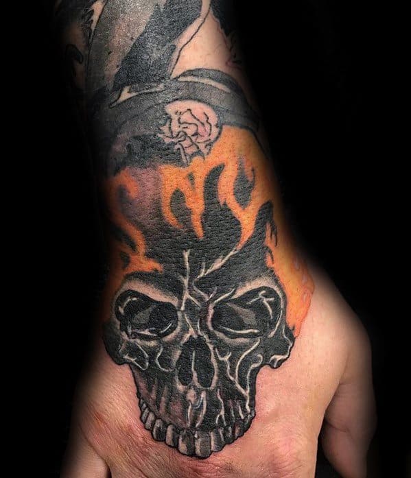 Ghost Rider hand tattoo featuring a bold black skull with vivid orange flames rising from the top in a striking design.
