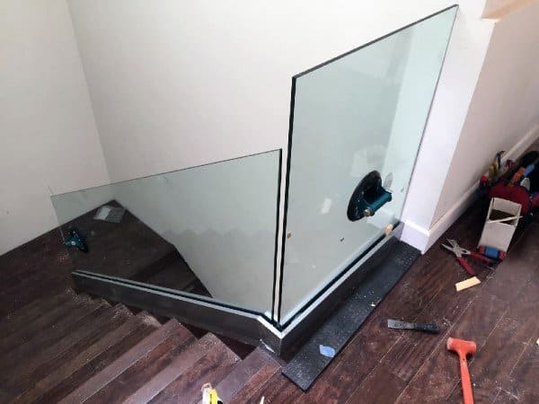 Staircase glass railing installation in progress with tools scattered on the wooden floor