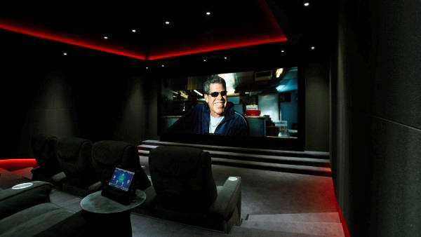 A chic home theater boasts a large screen with a sunglasses-clad figure, nestled among dark seating and red ambient lights