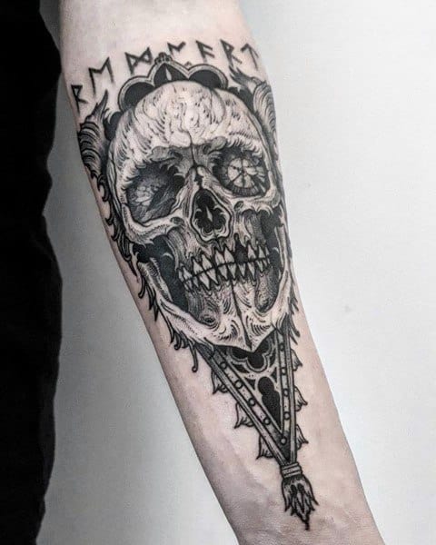 Black and grey forearm tattoo featuring a detailed skull with intricate patterns, gothic elements, and bold linework for a dark aesthetic.