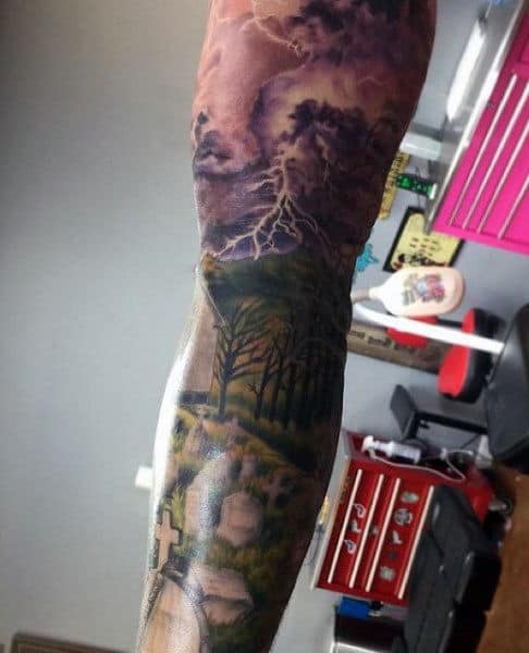 Tattoo of a stormy sky with lightning above a graveyard and forested landscape