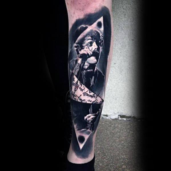 Realistic black and grey tattoo of Billie Joe Armstrong singing, with torn paper effect and handwritten lyrics across the arm.