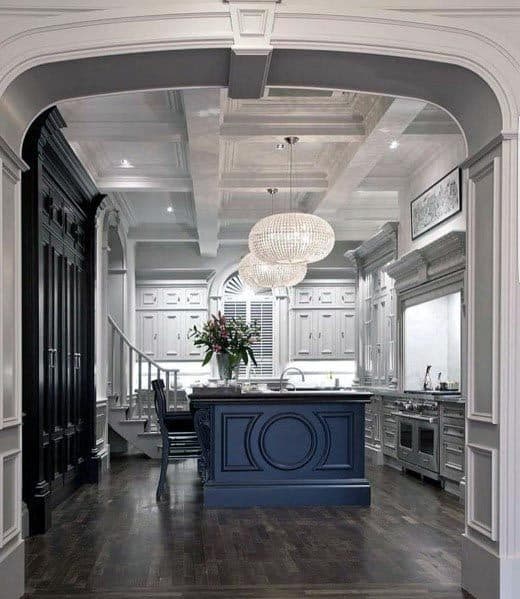 Elegant grey kitchen with navy island, coffered ceiling, and crystal chandeliers.