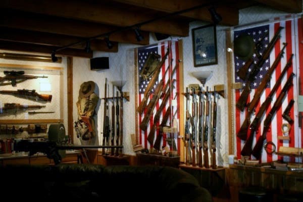Rustic gun room with American flag backdrops and a mix of rifles, gear, and decor.