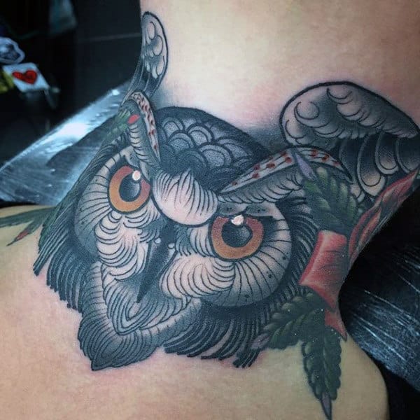 Throat tattoo of a detailed owl with piercing orange eyes, bold black shading, and intricate feather work, accented with red and green elements