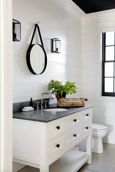 Modern half bath with round mirror, white vanity, black countertop, and potted plant featuring white shiplap walls and window