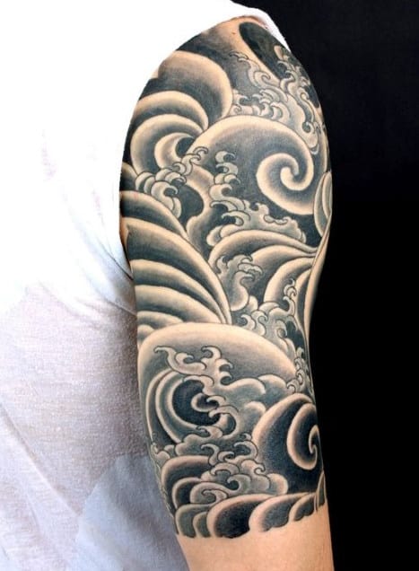 Black and gray waves tattoo sleeve on a person's upper arm, wearing a white shirt