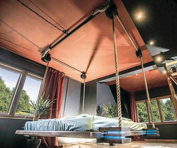 Modern hanging bed with sturdy rope supports, sleek wooden frame, and large windows in a stylish room.