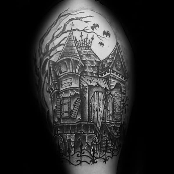 Upper arm tattoo of a haunted Victorian house with broken windows, full moon, flying bats, and twisted tree branches.