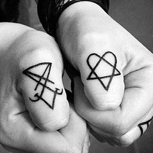 Two hands with tattoos on the thumbs: a geometric arrow on the left thumb and a heartagram design on the right thumb