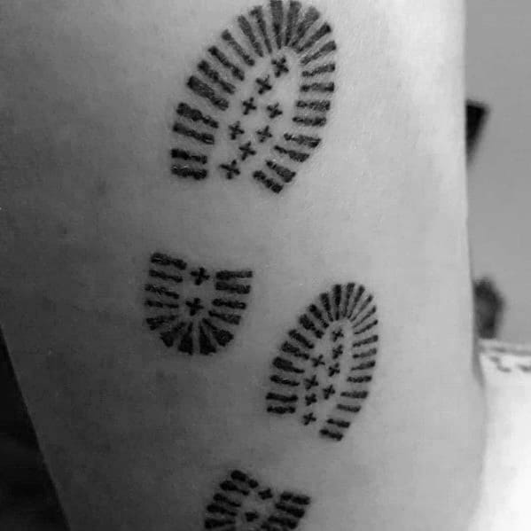 A black and gray tattoo of hiking boot prints, symbolizing adventure, exploration, and the journey of a hiker on the trail.