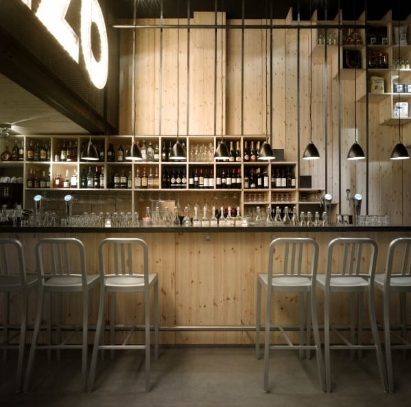 A modern bar featuring wooden decor, metal chairs, and pendant lights illuminating shelves of bottles