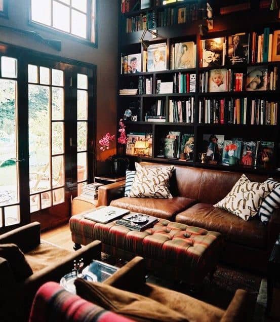 Cozy library with leather sofa, bookshelves, and a large window overlooking the lush garden