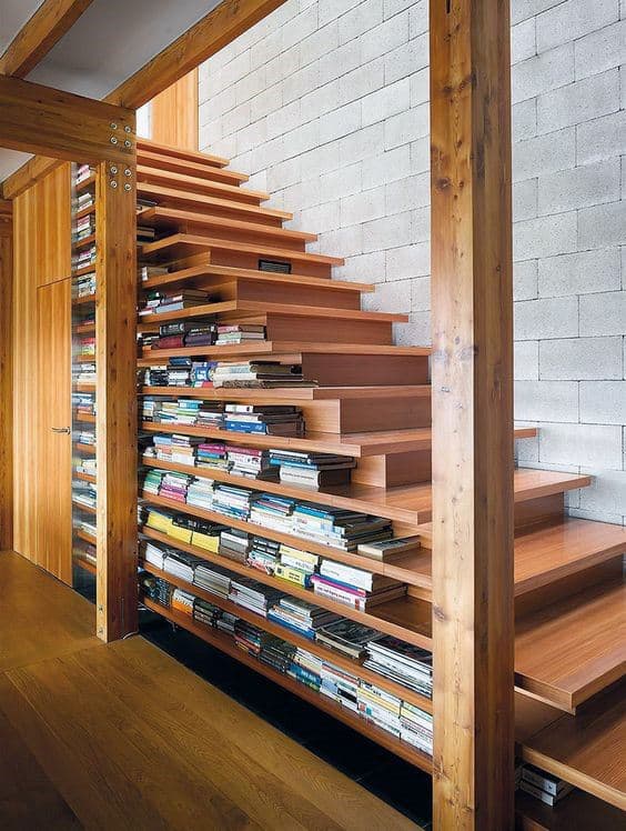 Wooden staircase with open steps filled like a library, alongside a white brick wall