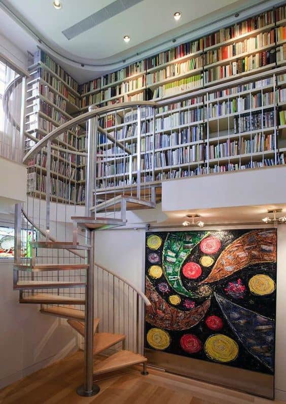 A spiral staircase leads to a vibrant two-story library with colorful abstract art on the wall
