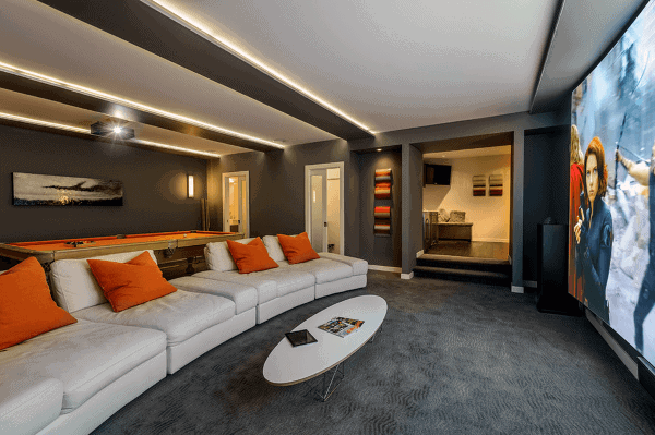 Home theater room featuring a large screen, white sectional sofa with orange pillows, and a pool table in the background