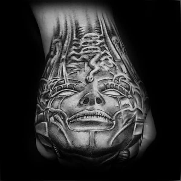 HR Giger-inspired hand tattoo showing a surreal biomechanical face with tubing, spine elements, and alien-like textures.