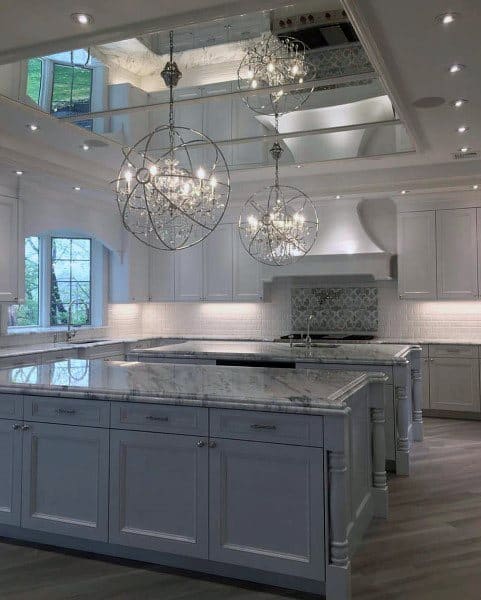 two gray islands in large kitchen with white cabinets and ceiling mirror 