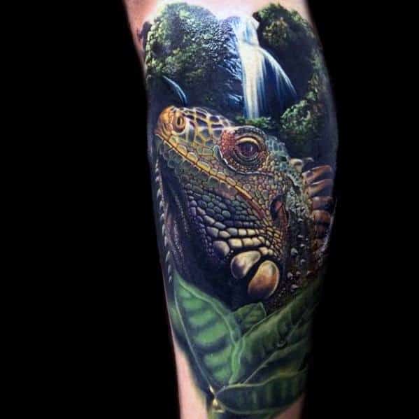 Realistic iguana tattoo with vivid jungle backdrop, lush green leaves, and a cascading waterfall above the reptile's head.