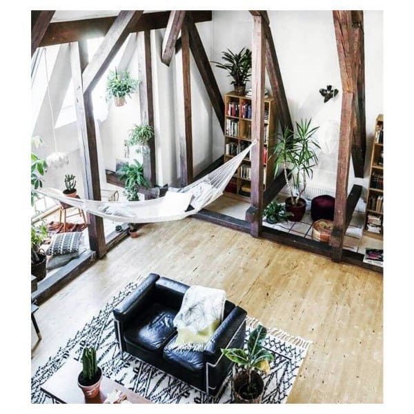 White hammock in a loft-style room with wooden beams, plants, and cozy seating area.