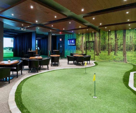 Indoor golf room with putting green, tables, chairs, forest wall mural, and ceiling lights