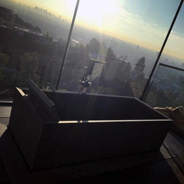 Bathtub with cityscape view, large windows, trees, and sunlight streaming in