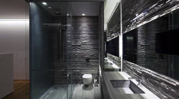 Modern bathroom with stone-textured walls, a glass shower, large mirror, and sleek fixtures