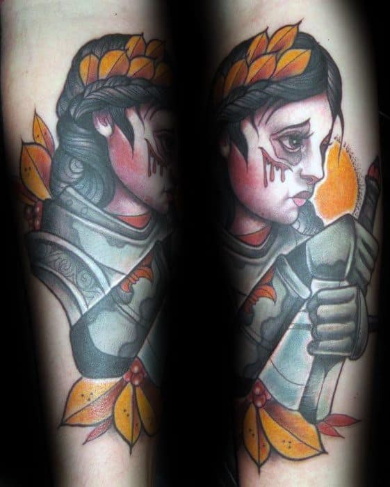 Neo-traditional Joan of Arc tattoo featuring bold outlines, vibrant orange-yellow tones, and a sorrowful expression in armor.