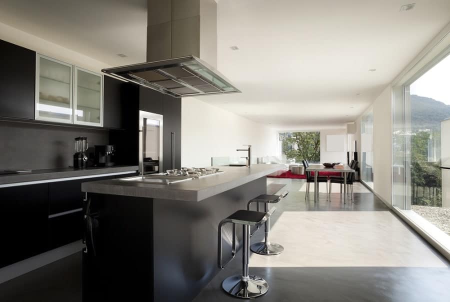 Sleek modern kitchen with black cabinets, stainless steel island, and bar stools; overlooks a dining area with large windows