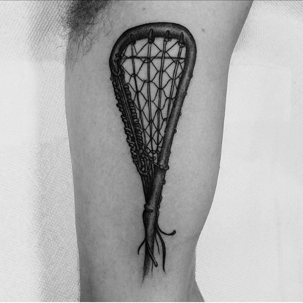 Realistic black and grey lacrosse stick tattoo with intricate netting detail, placed on the leg for a bold and athletic look.
