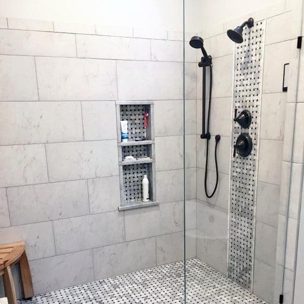 A modern shower with light gray tiles, a mosaic accent strip, built-in storage niches, and matte black fixtures.