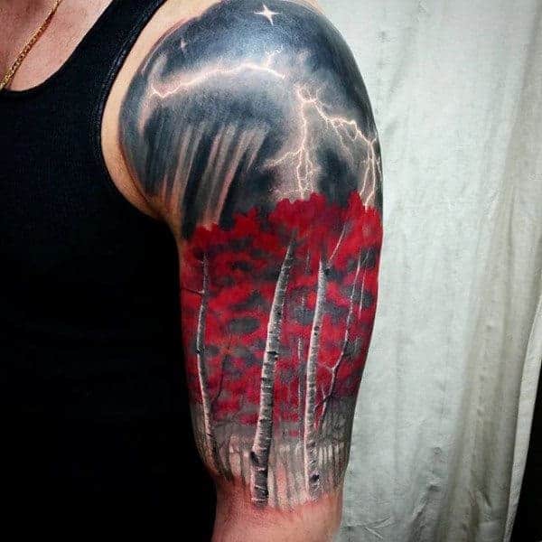 Upper arm tattoo depicting a stormy sky with lightning above red-leafed trees