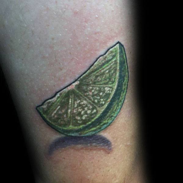 Realistic lime wedge tattoo with vibrant green shading and intricate details, featuring a shadow effect for a bold and lifelike appearance.