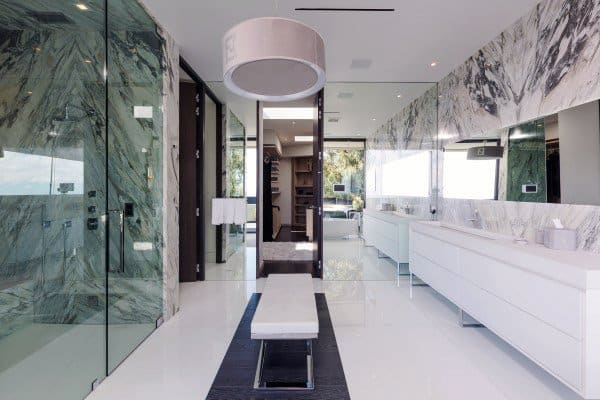 Modern bathroom with marble walls, large mirrors, a sleek shower, white cabinets, bench, and chandelier